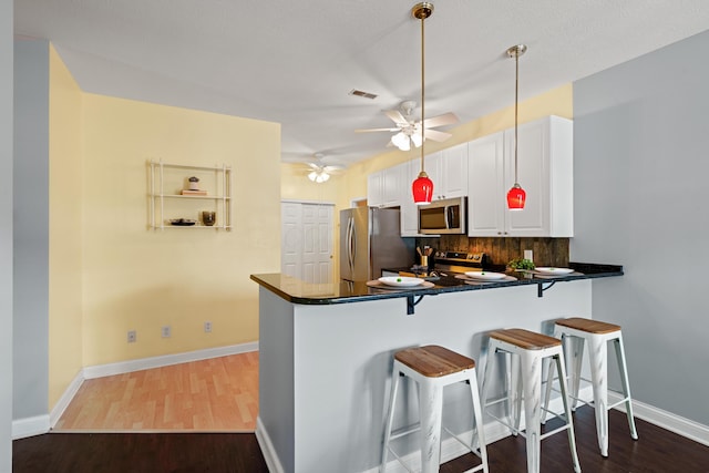 kitchen featuring dark countertops, a peninsula, white cabinets, and stainless steel appliances