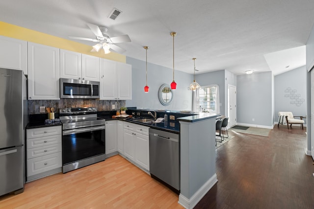 kitchen with white cabinets, dark countertops, a peninsula, stainless steel appliances, and a sink