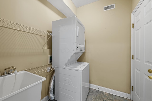 clothes washing area featuring visible vents, a sink, stacked washing maching and dryer, laundry area, and baseboards