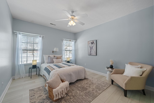 bedroom featuring a ceiling fan, light wood-style flooring, a textured ceiling, and baseboards