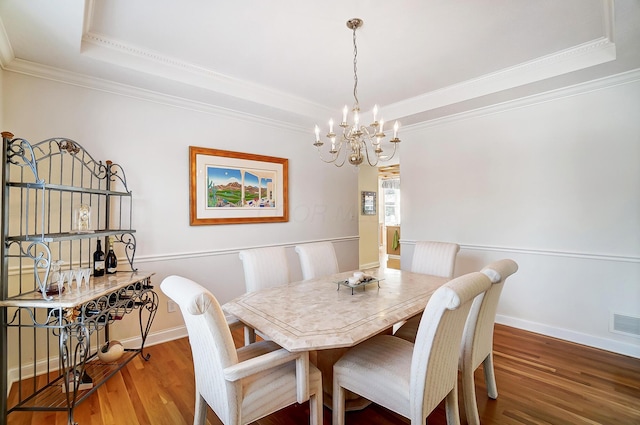 dining room featuring visible vents, a tray ceiling, wood finished floors, crown molding, and baseboards