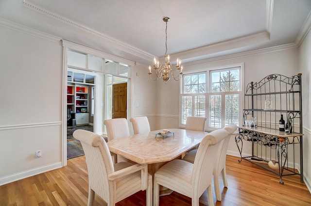 dining room featuring crown molding, light wood-type flooring, a tray ceiling, and a chandelier