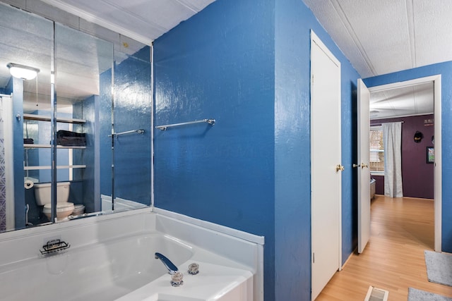 bathroom with toilet, a bath, a textured ceiling, and hardwood / wood-style flooring