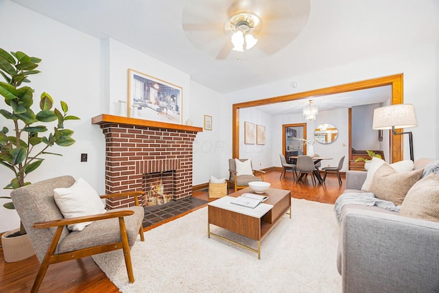 living room featuring wood-type flooring, ceiling fan with notable chandelier, and a fireplace