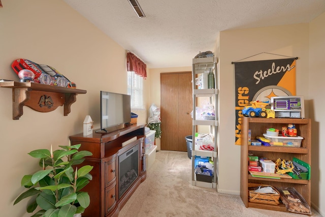 recreation room featuring a fireplace, visible vents, light colored carpet, and a textured ceiling