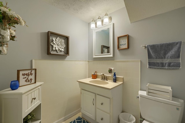 half bathroom featuring a wainscoted wall, vanity, tile walls, a textured ceiling, and toilet