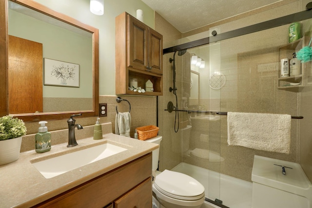 full bathroom featuring vanity, tile walls, a shower stall, a textured ceiling, and toilet