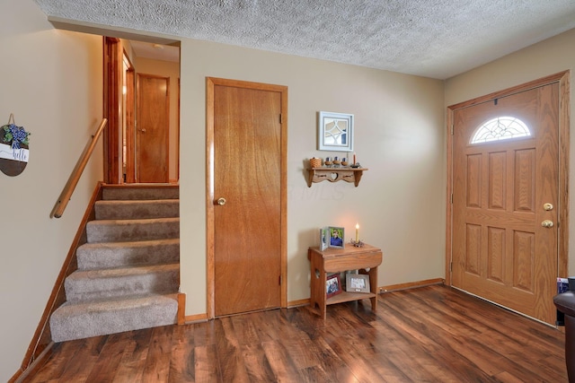 foyer entrance featuring a textured ceiling, stairs, dark wood-type flooring, and baseboards