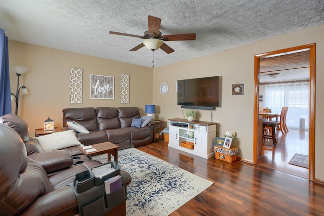 living area featuring a textured ceiling, dark wood-style floors, a ceiling fan, and baseboards