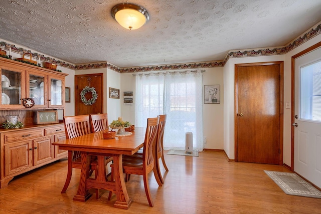 dining area with light wood-style flooring, a textured ceiling, and baseboards