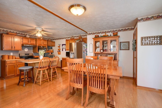 dining room with a ceiling fan, baseboards, light wood-style floors, and a textured ceiling