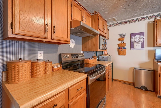 kitchen with under cabinet range hood, light countertops, light wood finished floors, a textured ceiling, and stainless steel appliances