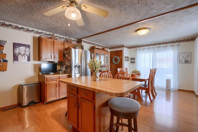 kitchen featuring brown cabinets, a kitchen island, wood counters, stainless steel refrigerator with ice dispenser, and light wood-type flooring