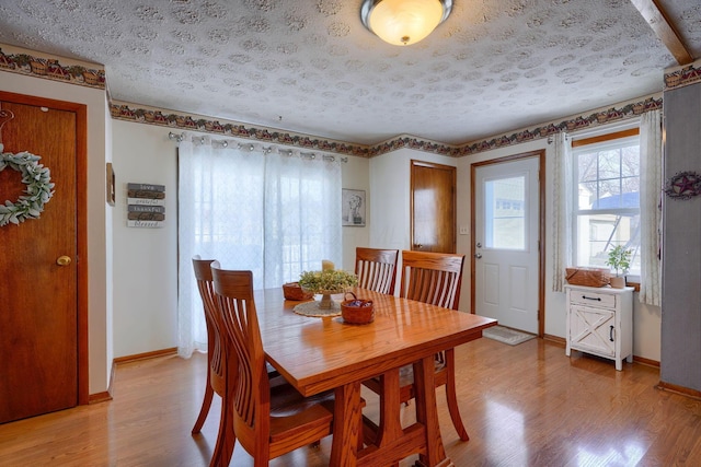 dining space with a textured ceiling, light wood finished floors, and baseboards