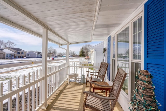 snow covered back of property with a residential view, a porch, and a sunroom