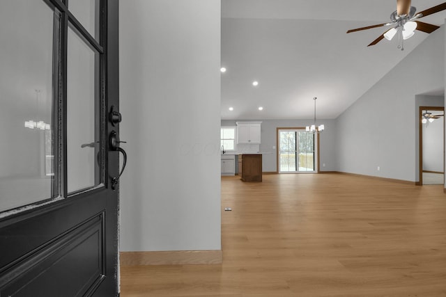 foyer with high vaulted ceiling, ceiling fan with notable chandelier, and light wood-type flooring