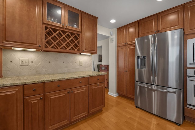 kitchen featuring tasteful backsplash, stainless steel appliances, light stone countertops, and light hardwood / wood-style floors