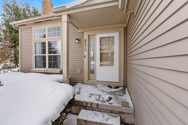 snow covered property entrance featuring a chimney