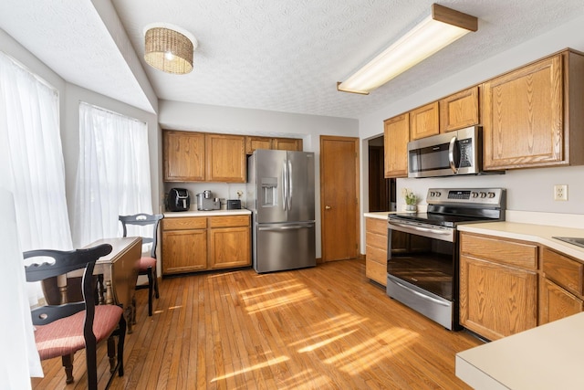 kitchen with light countertops, appliances with stainless steel finishes, brown cabinetry, a textured ceiling, and light wood-type flooring