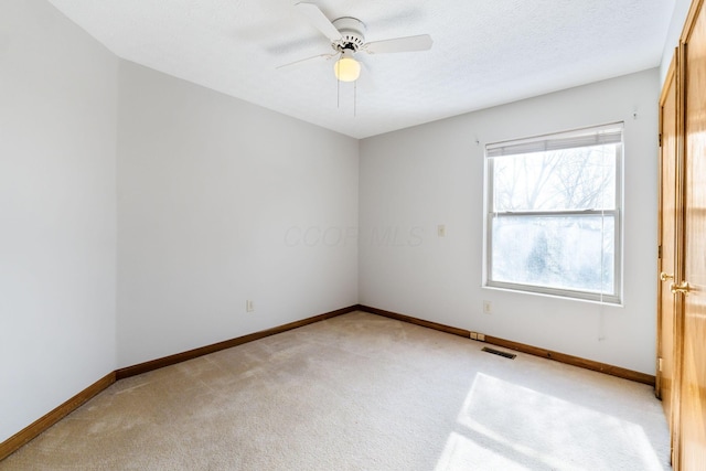 unfurnished room featuring ceiling fan, a textured ceiling, light colored carpet, visible vents, and baseboards