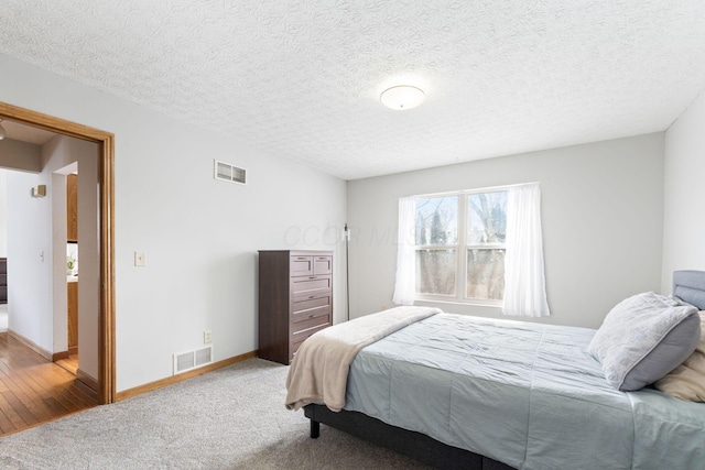 carpeted bedroom featuring baseboards, visible vents, and a textured ceiling