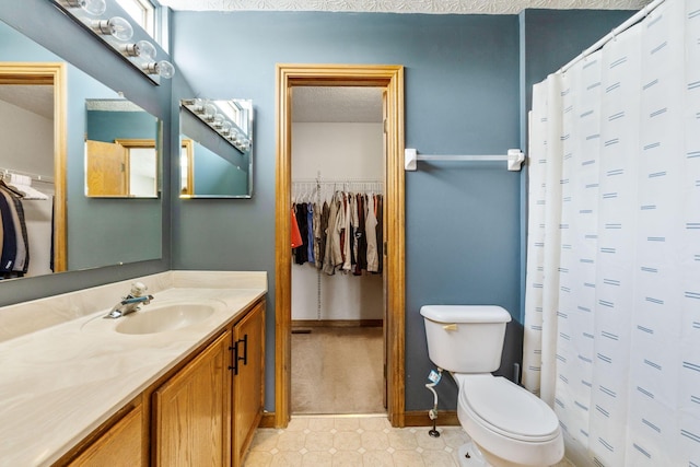 full bath featuring a textured ceiling, toilet, vanity, baseboards, and a walk in closet