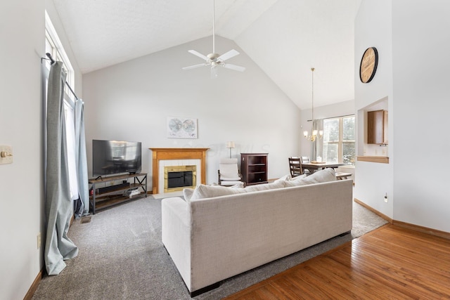 living room featuring high vaulted ceiling, ceiling fan with notable chandelier, wood finished floors, baseboards, and a tiled fireplace