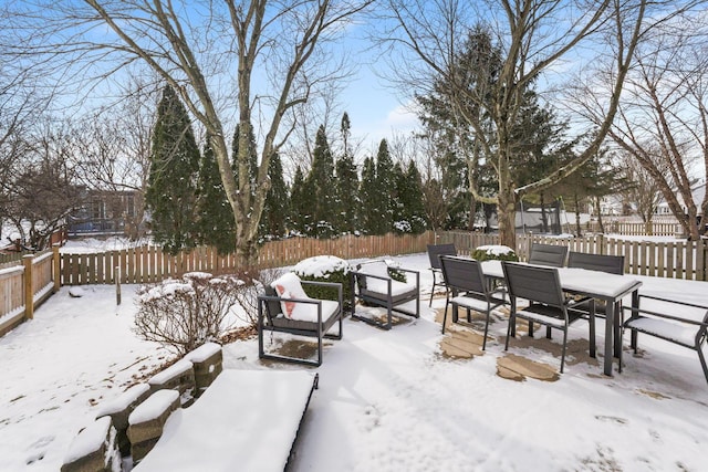 snow covered patio with outdoor dining space and a fenced backyard