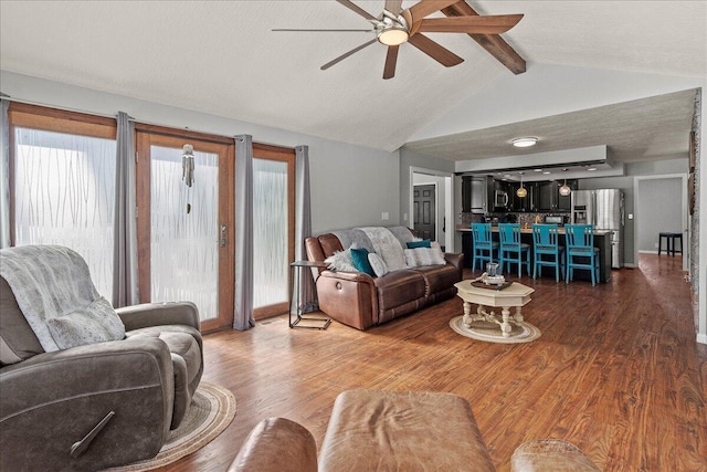 living room with a ceiling fan, wood finished floors, and vaulted ceiling with beams