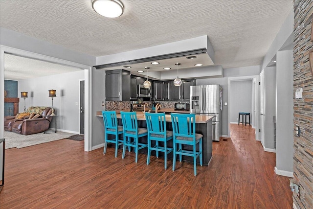 kitchen with dark wood finished floors, a large fireplace, a peninsula, a breakfast bar area, and appliances with stainless steel finishes