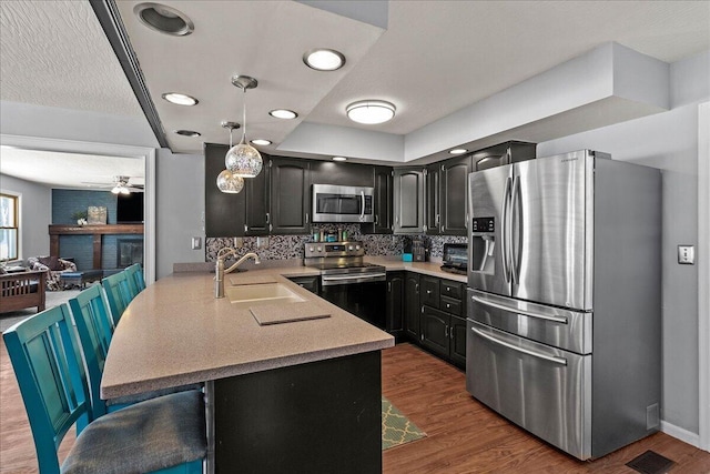 kitchen with a sink, dark wood-style floors, stainless steel appliances, a peninsula, and light countertops