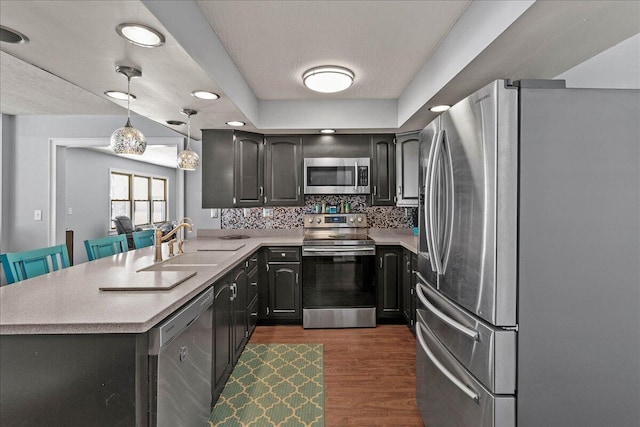 kitchen featuring appliances with stainless steel finishes, light countertops, a peninsula, and a sink