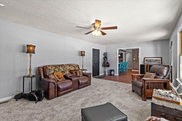 carpeted living room featuring a ceiling fan, baseboards, and a textured ceiling