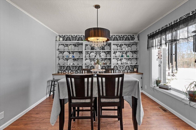 dining room with wood finished floors, visible vents, baseboards, a textured ceiling, and crown molding