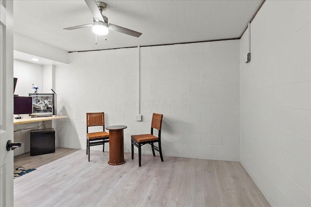 living area featuring a textured ceiling, concrete block wall, ceiling fan, and wood finished floors