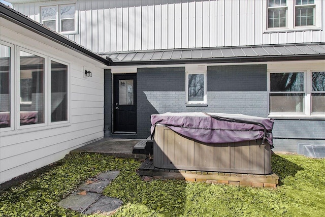 view of exterior entry with a standing seam roof, brick siding, and a hot tub