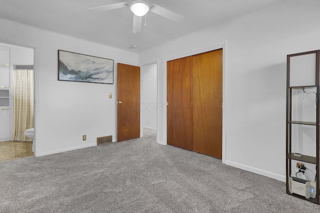 unfurnished bedroom featuring carpet floors, a closet, visible vents, ensuite bathroom, and a ceiling fan