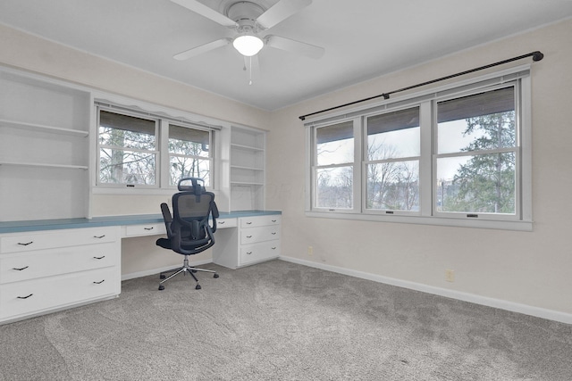 unfurnished office with built in features, built in desk, light carpet, ceiling fan, and baseboards