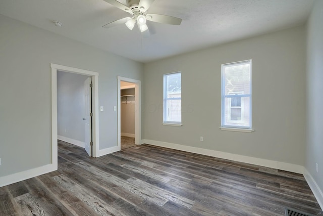 unfurnished bedroom with ceiling fan, dark wood-type flooring, a walk in closet, and a closet