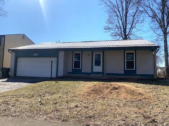 single story home with metal roof, driveway, covered porch, and an attached garage