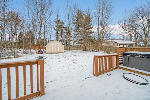 snowy yard with a shed, an outdoor structure, a wooden deck, and a hot tub