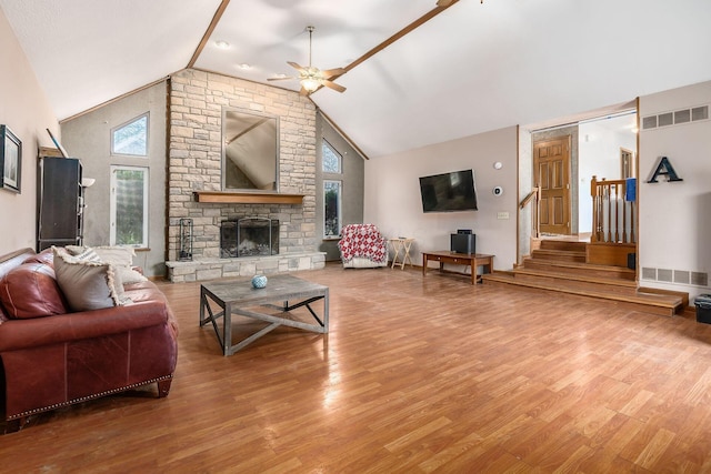 living area featuring visible vents, stairway, wood finished floors, a stone fireplace, and high vaulted ceiling