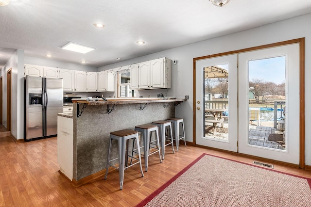 kitchen with white cabinets, stainless steel fridge, plenty of natural light, and a kitchen breakfast bar