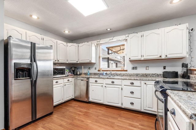 kitchen featuring stainless steel appliances, a sink, light wood-style flooring, and white cabinetry