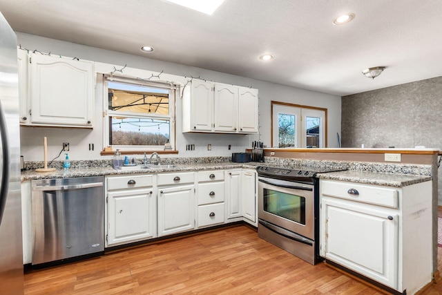 kitchen featuring light wood-style flooring, appliances with stainless steel finishes, a peninsula, white cabinetry, and a sink