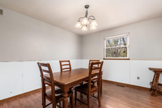 dining area with an inviting chandelier, visible vents, wood finished floors, and wainscoting