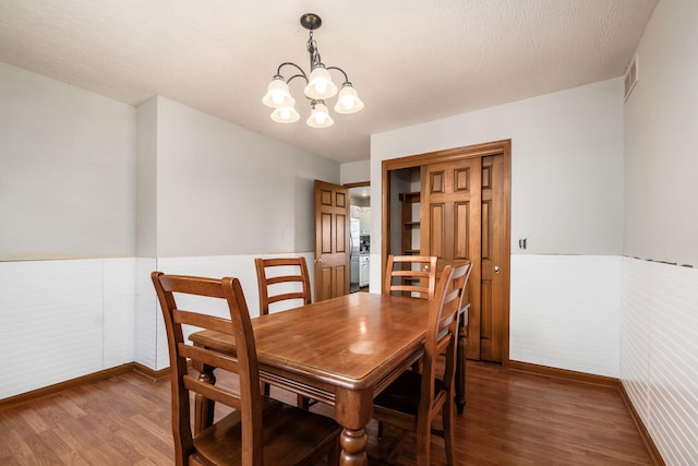 dining area featuring visible vents, wainscoting, wood finished floors, a textured ceiling, and a notable chandelier