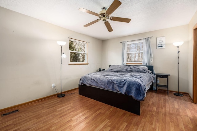 bedroom with light wood finished floors, baseboards, visible vents, and ceiling fan