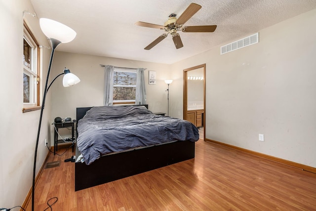 bedroom featuring visible vents, ensuite bathroom, a textured ceiling, light wood-type flooring, and baseboards