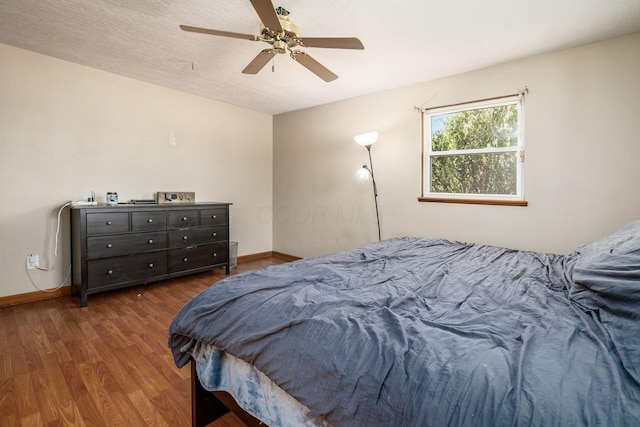 bedroom featuring ceiling fan, a textured ceiling, wood finished floors, and baseboards